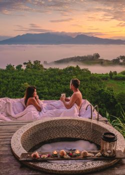 a couple of men and women in a bathtub looking out over the mountains of Northern Thailand during vacation. Outdoor bathroom, and bathtub during sunrise at the mountains of Nan with mist and fog